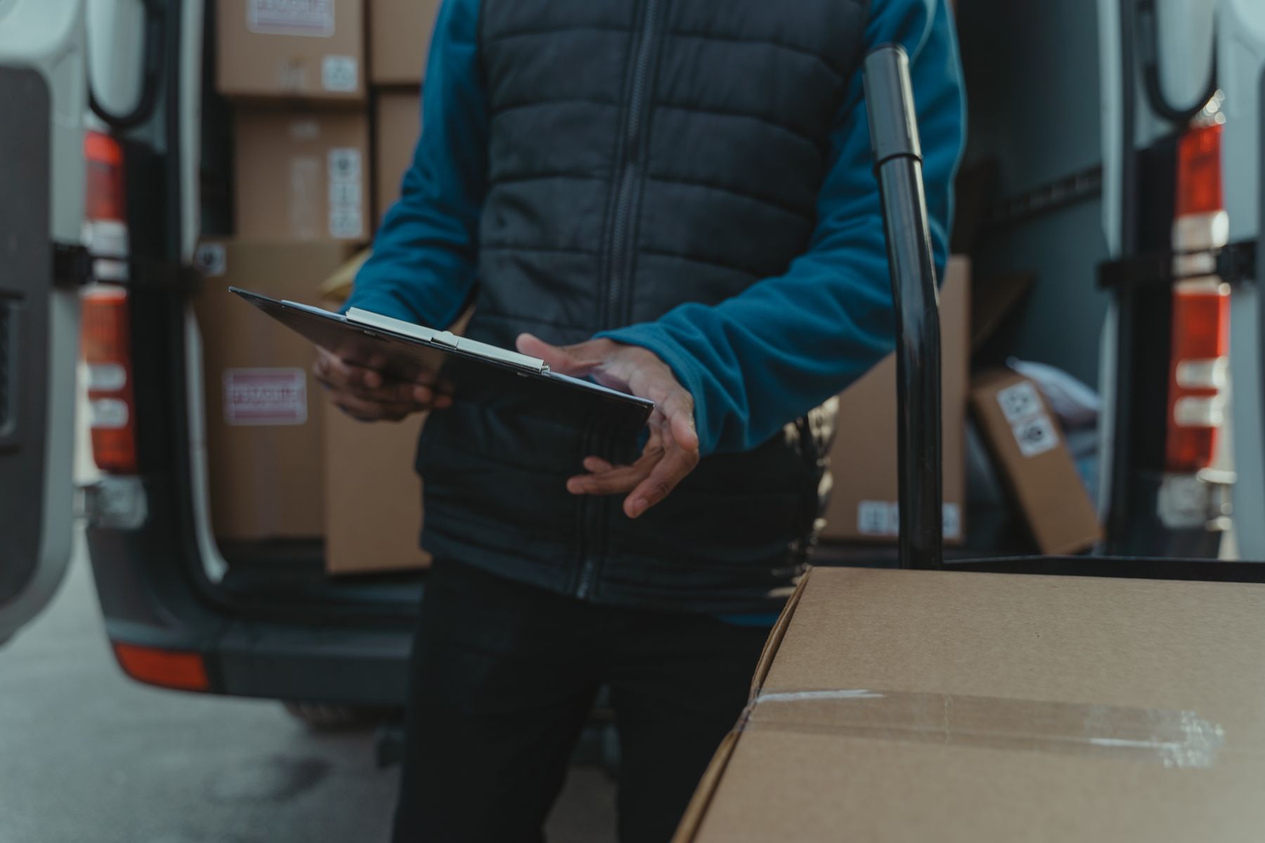 A courier reviewing delivery paperwork beside packages in a van